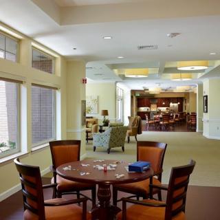 A cozy living room area with a round table and chairs, well-lit by natural light through large windows.