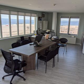 A modern office with a stunning ocean view, featuring desks and chairs.