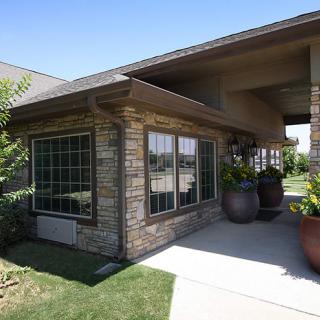 A modern house with a stone facade and large windows, surrounded by greenery on a sunny day.