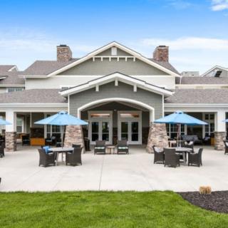 A modern building with outdoor seating on a sunny patio, surrounded by well-maintained landscaping.