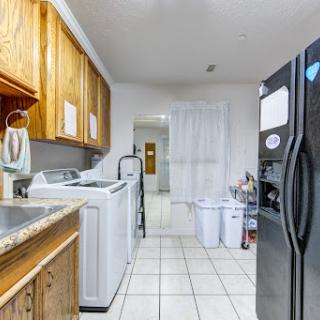 A functional kitchen featuring a refrigerator, washing machine, and dryer with wooden cabinetry.