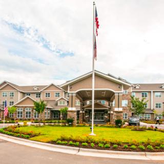 A large building with an American flag at the entrance, surrounded by a landscaped garden and a roundabout under a cloudy sky.