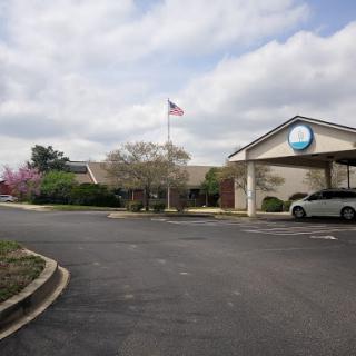 View of a building with an American flag waving in front, surrounded by greenery under a cloudy sky.