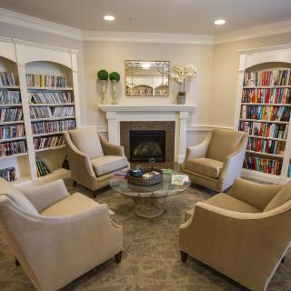 A cozy library room with comfortable seating around a fireplace and shelves filled with books.