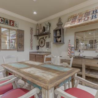 A rustic indoor dining area with nautical and cafe-themed decor, featuring a wooden table and chairs, American flags, and vintage-style decorations.