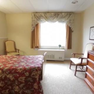 A cozy bedroom with floral bedding, a large window, and classic furniture.