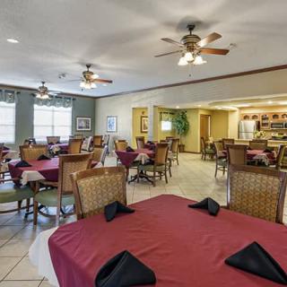 A casual dining room with tables set up for guests, featuring ceiling fans and natural lighting.