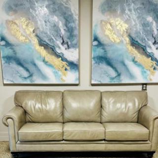 A cozy beige leather sofa placed beneath two abstract paintings in a living room setting.