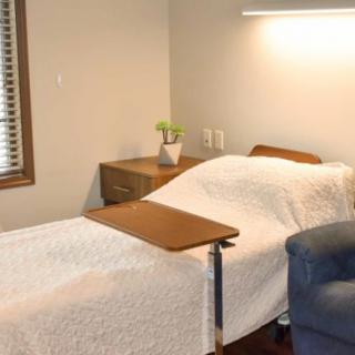 A hospital room with a bed, chair, and table beside a window.