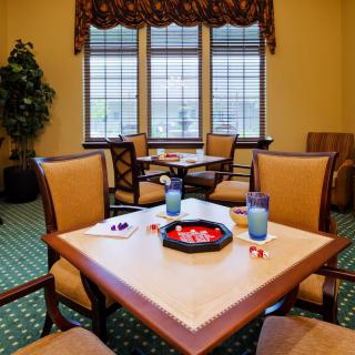 A cozy dining area with tables and chairs, featuring decorative windows and a green carpet.