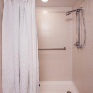 A clean and minimalist shower area featuring a white curtain and supportive grab bar.