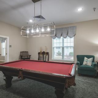 A cozy billiards room featuring a red pool table, elegant lighting, and classic furnishings.