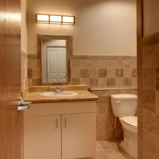 A well-lit bathroom featuring a sink, mirror, and toilet with tiled walls and flooring.