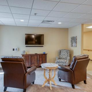 A cozy living room with leather chairs, a small round table, and a television mounted on the wall.