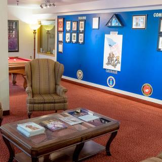 A cozy lounge area with a wingback chair and coffee table, featuring artwork on a blue wall.