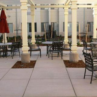 An outdoor patio with tables and chairs under a pergola, featuring red umbrellas.
