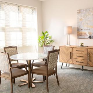 A bright dining area with a round table, modern wooden furniture, and natural light streaming through large windows.