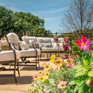 A sunny patio with comfortable outdoor seating surrounded by vibrant flowers.
