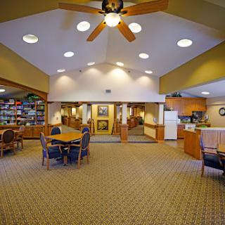 A spacious and welcoming common area featuring a dining space with tables and chairs, a ceiling fan, and an adjacent kitchen.
