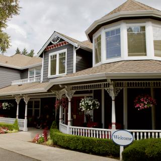A large, traditional-style house with a welcoming front porch and hanging flower baskets.