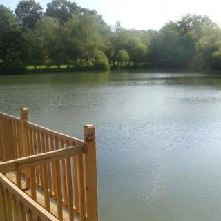 A serene view of a lake surrounded by trees, with a wooden railing in the foreground.