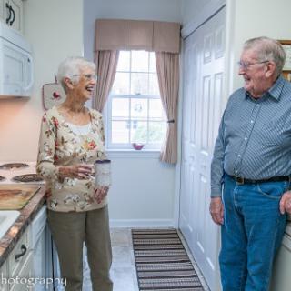 An elderly couple enjoys a lighthearted conversation in their cozy kitchen.