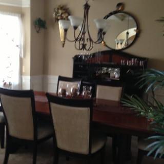 A cozy dining room featuring a wooden table, upholstered chairs, a mirror, and a chandelier.