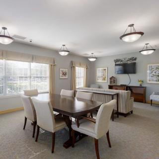 A well-lit dining room with a large table and upholstered chairs, featuring elegant lighting fixtures and decor.