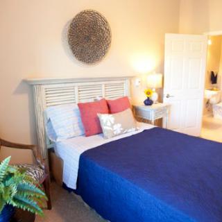 A cozy bedroom featuring a neatly made bed with a blue blanket and decorative pillows, complemented by warm lighting and tasteful decor.