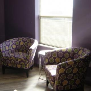 Two patterned armchairs sit in a sunlit room with purple walls and a window covered by blinds.