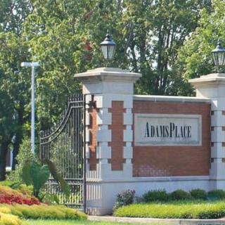 Entrance gate to a residential area with a sign and well-maintained landscaping.