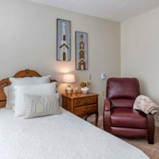 A cozy bedroom with a bed, nightstand, lamp, and a recliner chair.