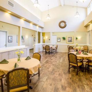 A bright and spacious dining room with neatly arranged tables and chairs, featuring wooden flooring and elegant decor.