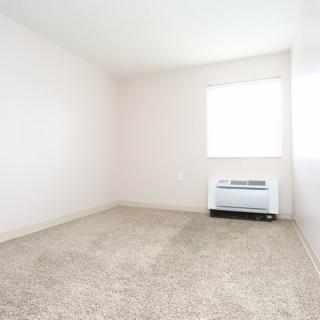 A small, empty room with carpeted flooring and a window letting in natural light.