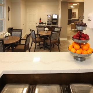 A cozy dining area with tables, chairs, and a fruit bowl on the counter.