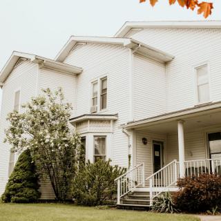 A charming white house with a front porch surrounded by trees and greenery.