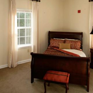 A cozy bedroom with a wooden bed frame, bedside table, and a window with curtains.