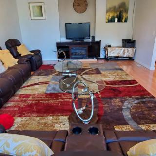 A cozy living room with a large patterned rug, glass coffee table, and comfortable seating facing a television.
