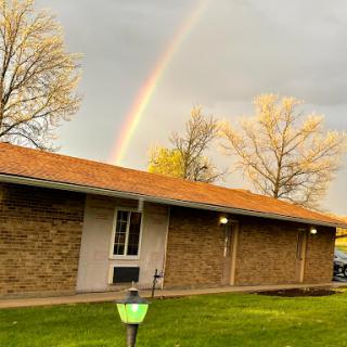 A beautiful rainbow arches over a cozy building, surrounded by a vibrant landscape.