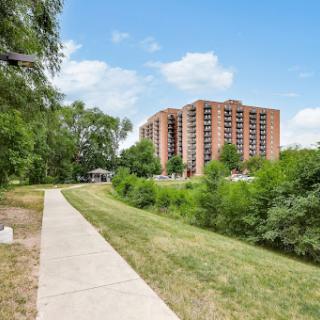 A scenic view of a residential building alongside a pathway bordered by lush greenery.