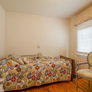 A cozy bedroom with a single bed covered in colorful bedding, an armchair by the window, and hardwood flooring.