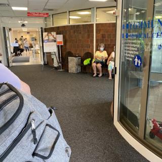A waiting area in a healthcare facility where individuals are seated, some wearing masks.