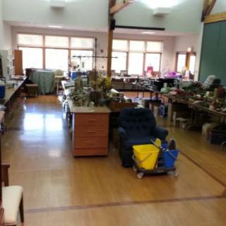 A spacious room filled with various furniture and decorative items, illuminated by large windows.