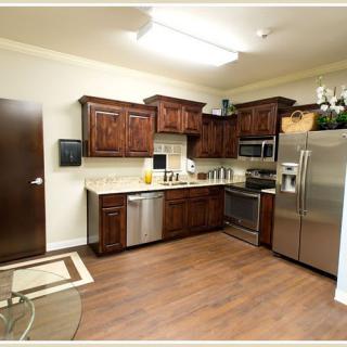 A modern kitchen with wooden cabinets and stainless steel appliances, featuring a hardwood floor.