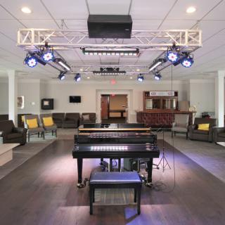 A modern lounge area featuring a piano and stage lighting, surrounded by comfortable seating.