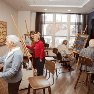 A group of seniors participating in an art class, painting on canvases set up on easels.