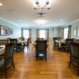 A well-lit dining room with wooden floors, arranged with multiple tables and chairs.
