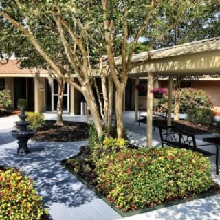 A tranquil courtyard garden with trees, bushes, benches, and a small fountain.
