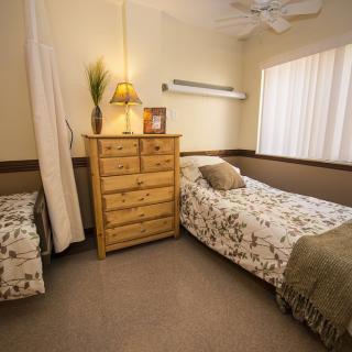 A cozy bedroom featuring twin beds with floral bedding, a wooden dresser, and warm lighting.