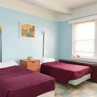 A cozy bedroom with two twin beds featuring purple bedspreads against light blue walls.